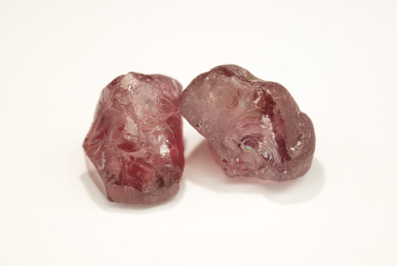 Two rough pink gemstones on a white background